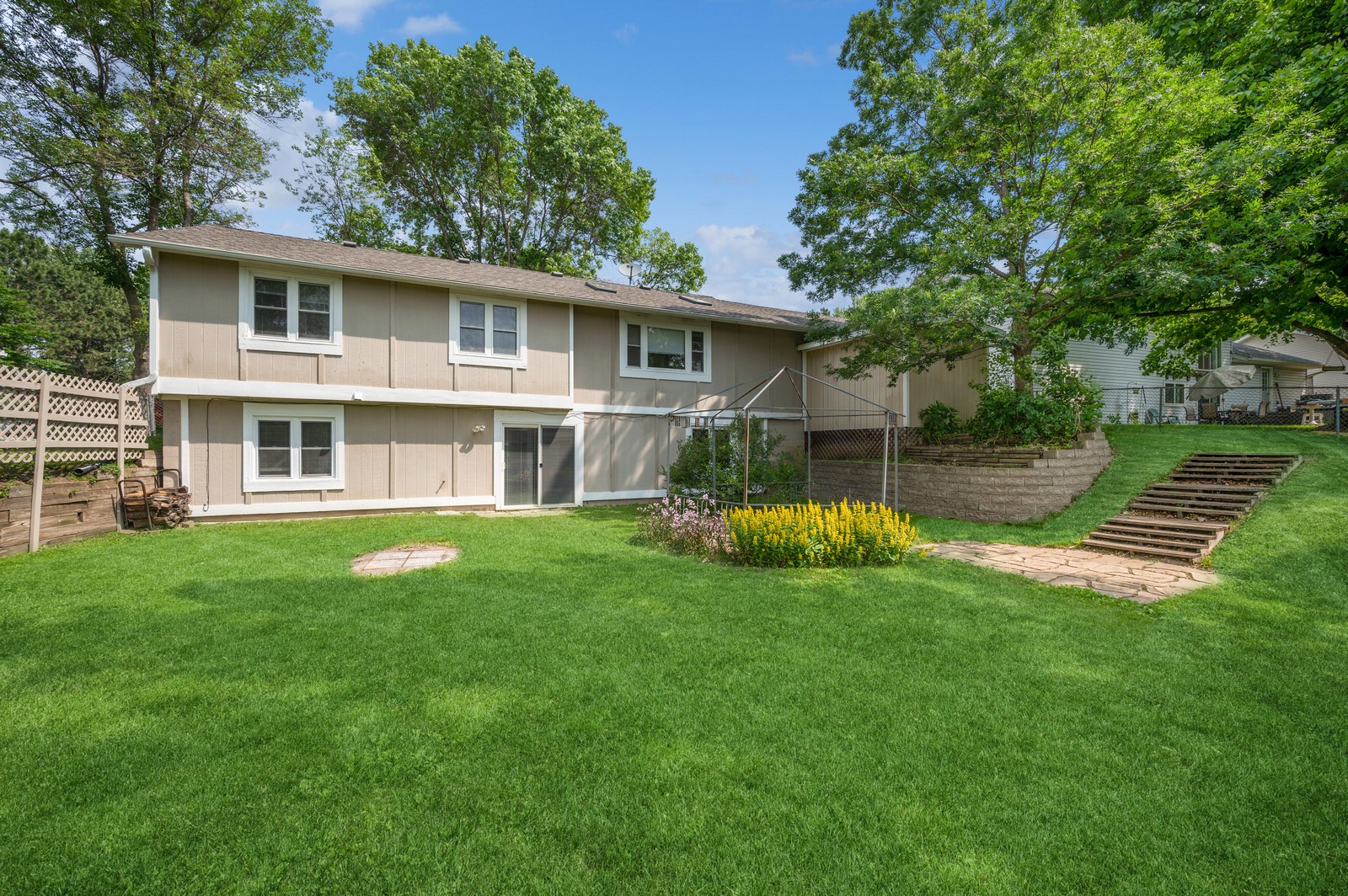 Backyard view of Blossom Hill Assisted Living in Woodbury, MN, showing the house with a patio and green lawn